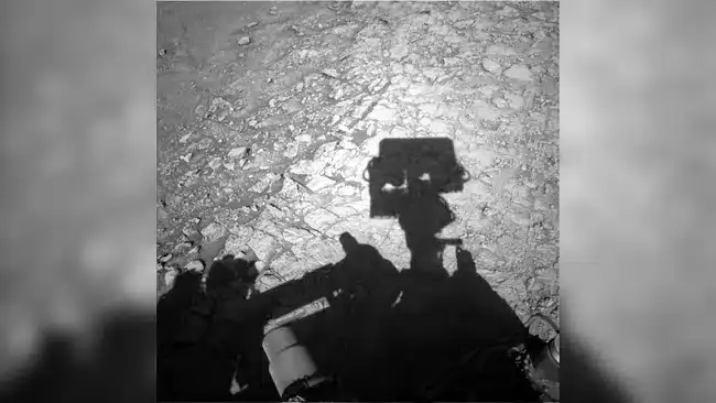 The-image-shows-Curiositys-shadow-stretching-across-the-ridged-boxwork-terrain-on-Mars-1a0b50ed159334a36bc09c7e01aaec24.webp